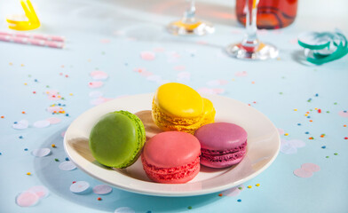 Birthday party concept. Colorful macaroons on the white plate, Glasses and wine bottle on the background.