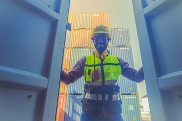 Smiley African American worker male in safety uniform,hard helmet and vest open container door in emport export logistic site