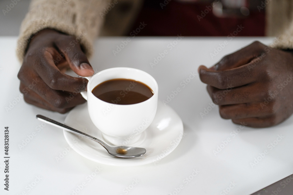 Wall mural close up hands of african american man holding cup of coffee wearing beige sweater. drops of coffee 