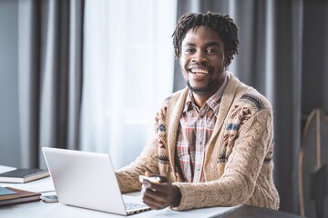 African man working from home using laptop sitting next to the window. Young entrepreneur working on his laptop at home. African american student study at home during lockdown