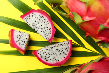 Slices of delicious white pitahaya fruit with palm leaf on yellow background, flat lay