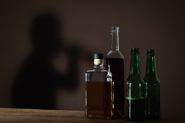 Obraz na płótnie Canvas Alcoholic drinks on wooden table against brown wall with shadow of addicted man