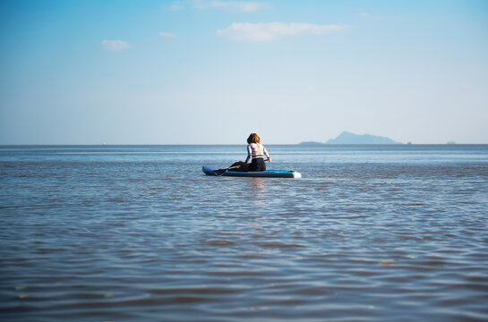 Young Asian Woman With Wetsuit Swimming Looking Forward On Sitting Paddle Board.