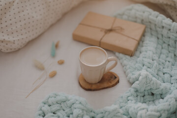 Fototapeta na wymiar Cup of coffee and a gift on the bed with white linens and blanket. Morning coffee in bed concept.
