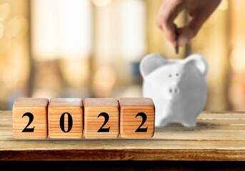Text of 2022 number written on wooden blocks with blur of coins and pink piggy bank