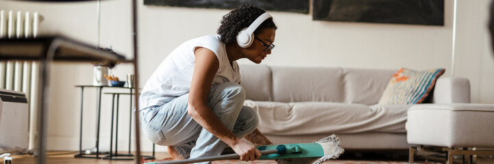 Woman with vitiligo wearing headphones using mop while cleaning floor