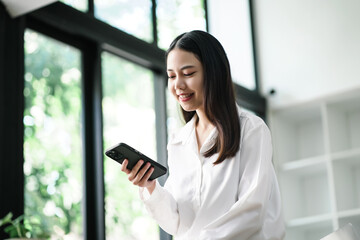 Young Asian woman smiling and happily looking at her mobile phone.