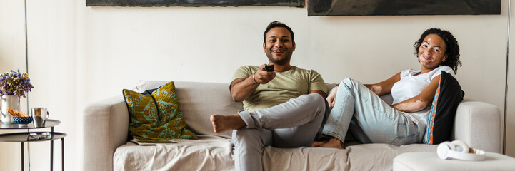 Middle eastern man and woman watching TV while resting on couch at home