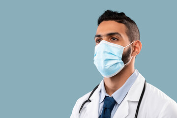Arabic Male Doctor Wearing Face Mask Looking Aside, Blue Background