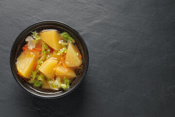 Bowl of tasty turnip soup on black table, top view. Space for text
