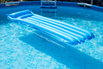 Blue inflatable mattress floating in a circular frame pool of a country house. The pool has the purest blue water.