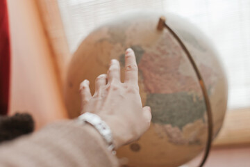hand pointing location on a vintage globe. Neutral color globe as home decor for kids room