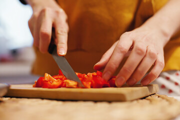 Woman chopping red bell pepper on cutting board in the kitchen preparing salad or cooking healthy dinner from vegetables. Vegan helathy lifestyle.