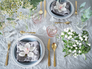 Spring vibe table setting with flowers: Linen napkins, linen tablecloth, golden cutlery and orchid flowers on the napkins