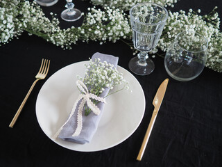 Table setting for a dinner, black tablecloth and white flowers