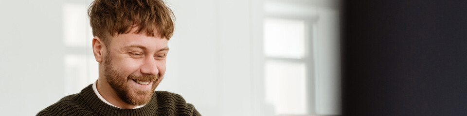 Obraz premium Young ginger man working with laptop while sitting at table in office