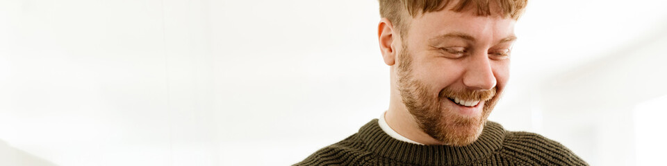 Obraz premium Young ginger man smiling and working with laptop while standing in office