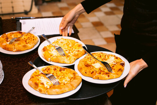 khachapuri with traditional georgian bread on a wooden board. The waiter serves khachapuri in a restaurant or diner.