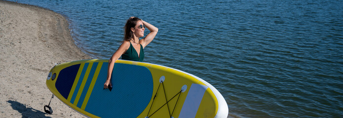 Caucasian woman walks along the beach and carries a sup board on the river in the city. Summer sport.