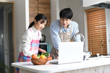 ノートパソコンを見ながら一緒に料理をする男女（夫婦・カップル）