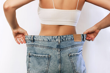 Cropped shot of a young slender tanned woman standing with her back dressed in wide jeans and white...