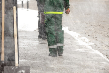 Public worker service putting salt on icy sidewalk during heavy snowfall.