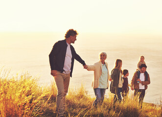 Say yes to adventure. A multi-generational family walking up a grassy hill together at sunset with...