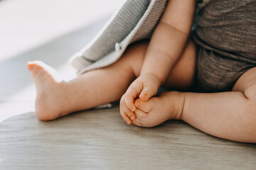 Closeup of barefoot feet of a baby sitting on a parquet floor at home.