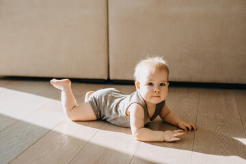 Barefoot baby crawling on a parquet floor at home, smiling, looking at camera.