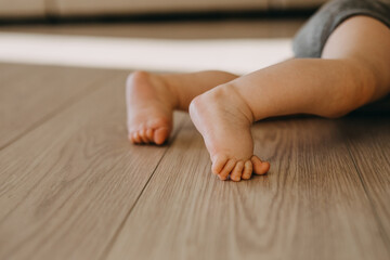 Closeup of barefoot baby feet on a wooden floor at home.