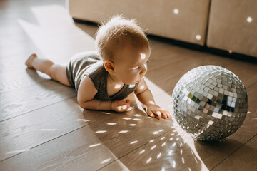 Curious baby playing with a disco ball in sun light.
