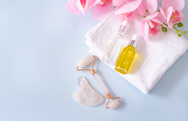 Quartz jade roller, Gua Sha massager with massage oil and towel on a blue background. Massage tool for facial skin care, the concept of SPA treatments