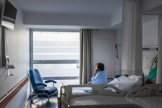 Patient woman sitting on bed in hospital and talking smartphone