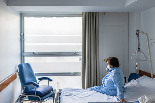Patient woman sitting on bed in hospital and talking smartphone