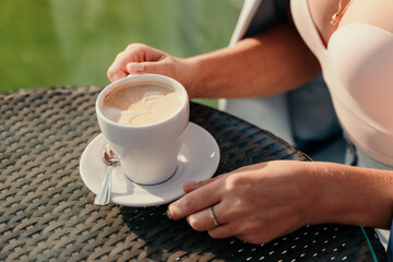Horizontal closeup shot of a young woman sitting in a cafe holding a cup of latte. Indoor lifestyle portrait of unrecognizable girl holding beautifully decorated latte art coffee.
