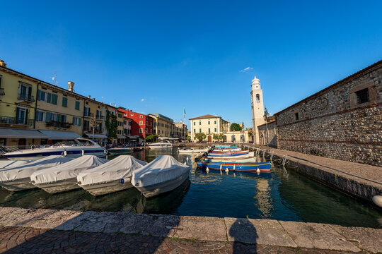 Small port of the Lazise village with moored boats. Tourist resort on the coast of Lake Garda (Lago di Garda). Verona province, Veneto, Italy, Europe. Ancient church of San Nicolo in Romanesque style.