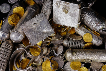 A lot of stacked gold bullion bars and gold coins and silver coins in a treasure sack. Treasure background. 
gold and silver jewelry. Ancient treasure. Pirate treasure and gold and silver filled crate