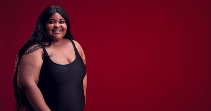 smiling young plus size woman in swimsuit posing on red background. diverse beauty