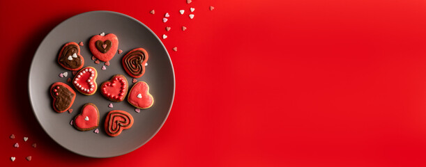 Top view of cookies in shape of hearts decorated by pink icing and sprinkles on grey plate on solid red background