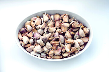 Large quantity of garlic cloves inside oval container on white background. Top view