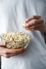 young man in a white t-shirt holding a glass large bowl of popcorn close-up