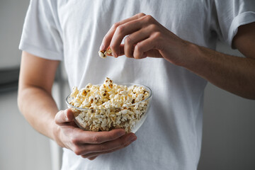 young man in a white t-shirt holding a glass large bowl of popcorn close-up