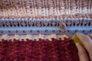 Close up of loom knit, with a person using loom hook, to create a pink and red blanket.