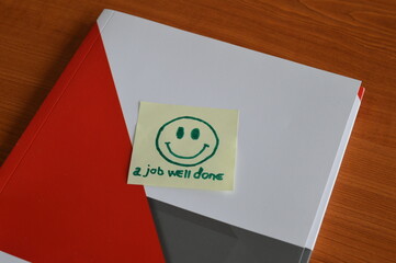 workbook with the message job well done and a smiling face, on the office desk, support and a positive response to good work, concept