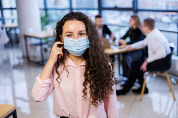 Fototapeta premium Young woman businesswoman in a mask working in the office during the coronavirus pandemic.
