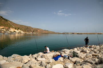 Fototapeta na wymiar Castellammare del Golfo, Trapani province, Sicily, Italy - Scenic view of the marina with two fishermen with fishing rods