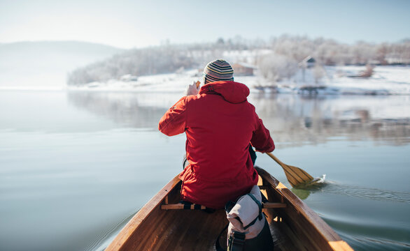Rear view of man in red jacket paddling canoe on lake winter ride