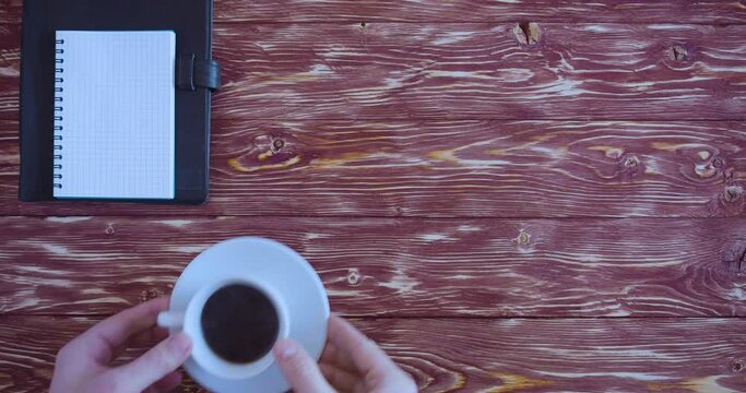 Top view - male hands put a cup of coffee, a spoon, a pen and a notepad with goals 2023 on a wioden vontage table.