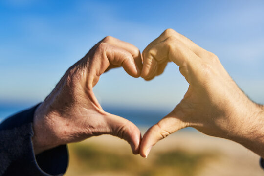 Father's day love concept. Care for the elderly concept. Old wrinkled male hand and young hand form heart shape at the beach
