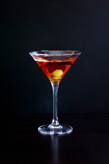 A glass of red martini with olives on a dark background. vertical photo